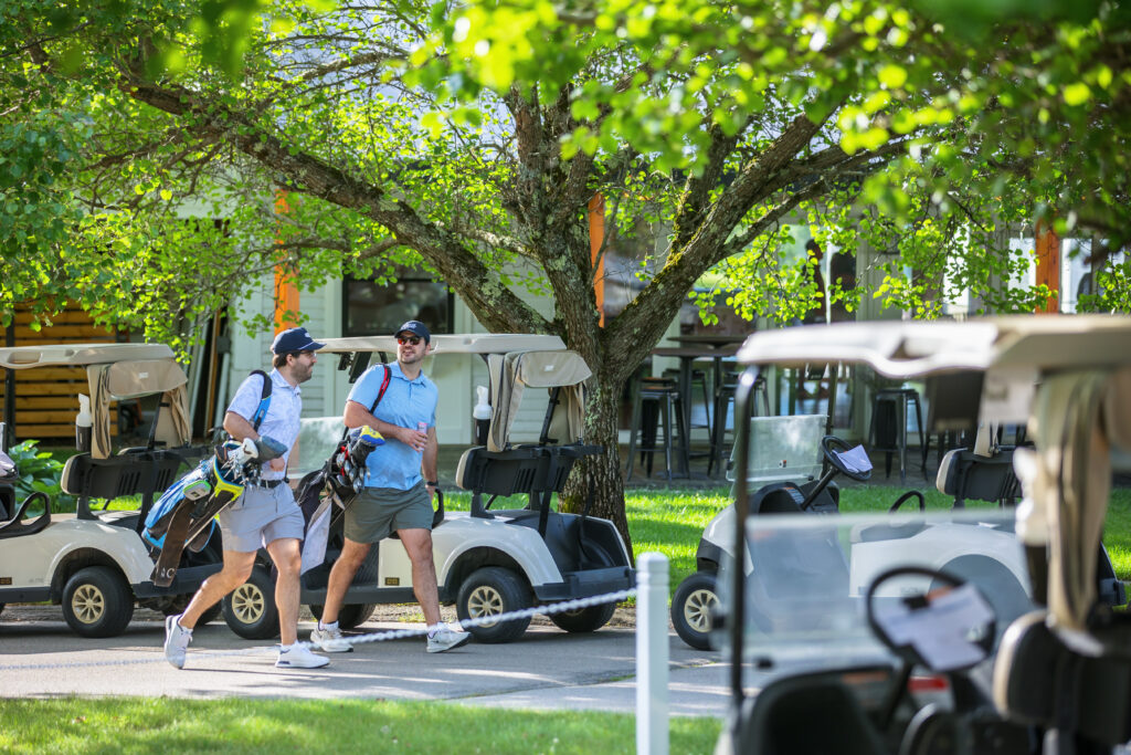 Two golfers with bags among golf carts near the clubhouse at Candia Woods Golf Links